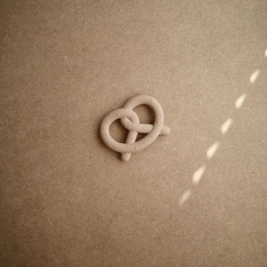 Tan silicone pretzel teether on cardboard background with natural sunlight highlights