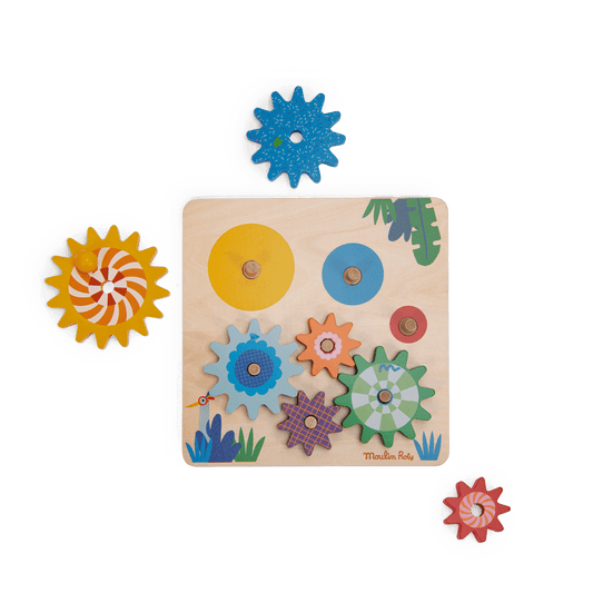 Partially assembled Moulin Roty wooden gear game board with loose colorful cogs on white background