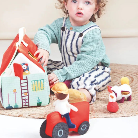 Toddler playing with Lilliputiens fabric farm house and red tractor on woven mat