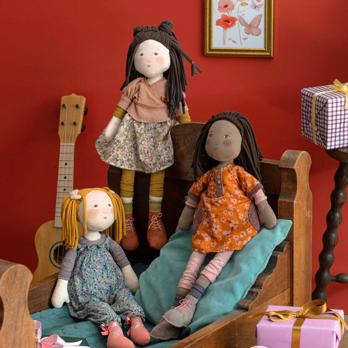 Three Camelia fabric dolls playing on a wooden bed frame with ukulele and gifts