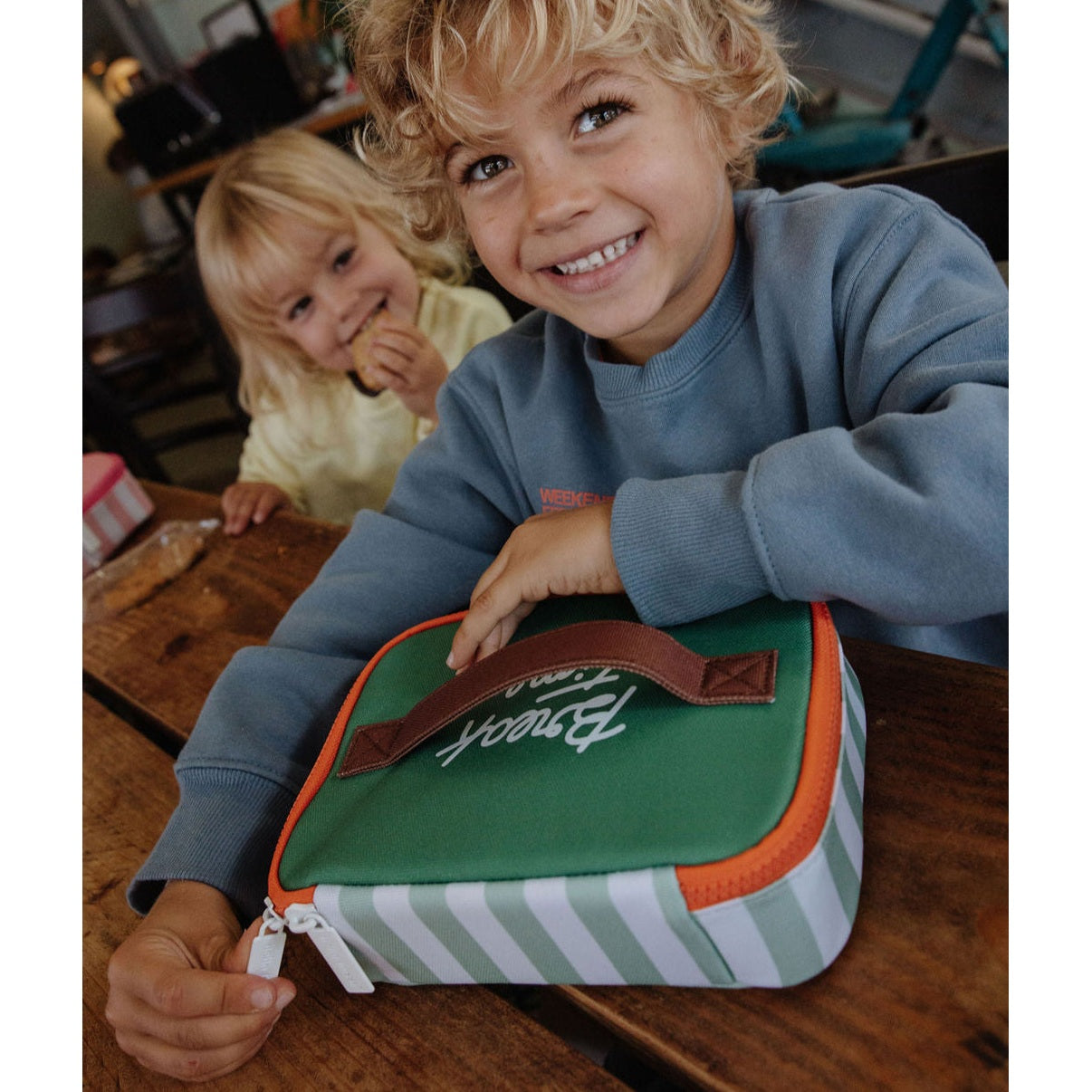Child holding green striped insulated lunch bag for school or outdoor use