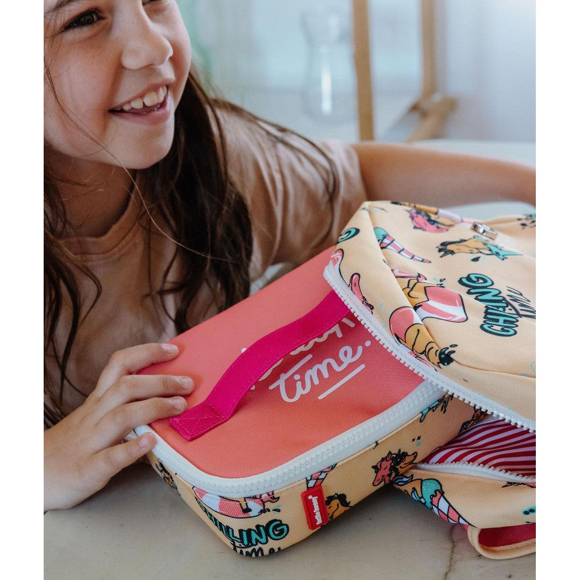 Smiling girl beside open unicorn lunch bag with red striped interior