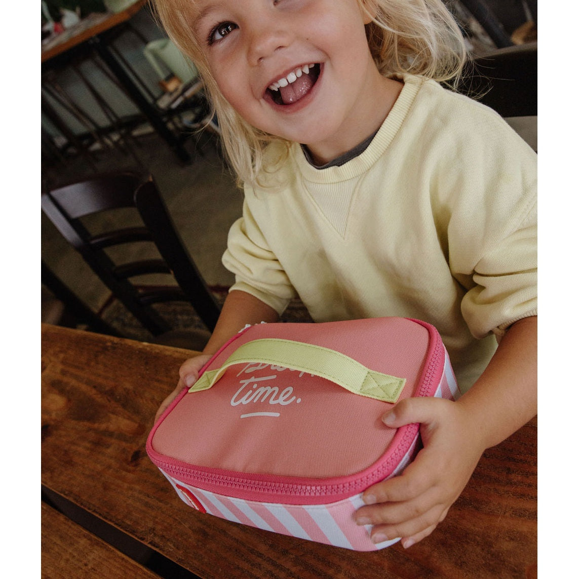 Child holding pink striped insulated lunch bag on table