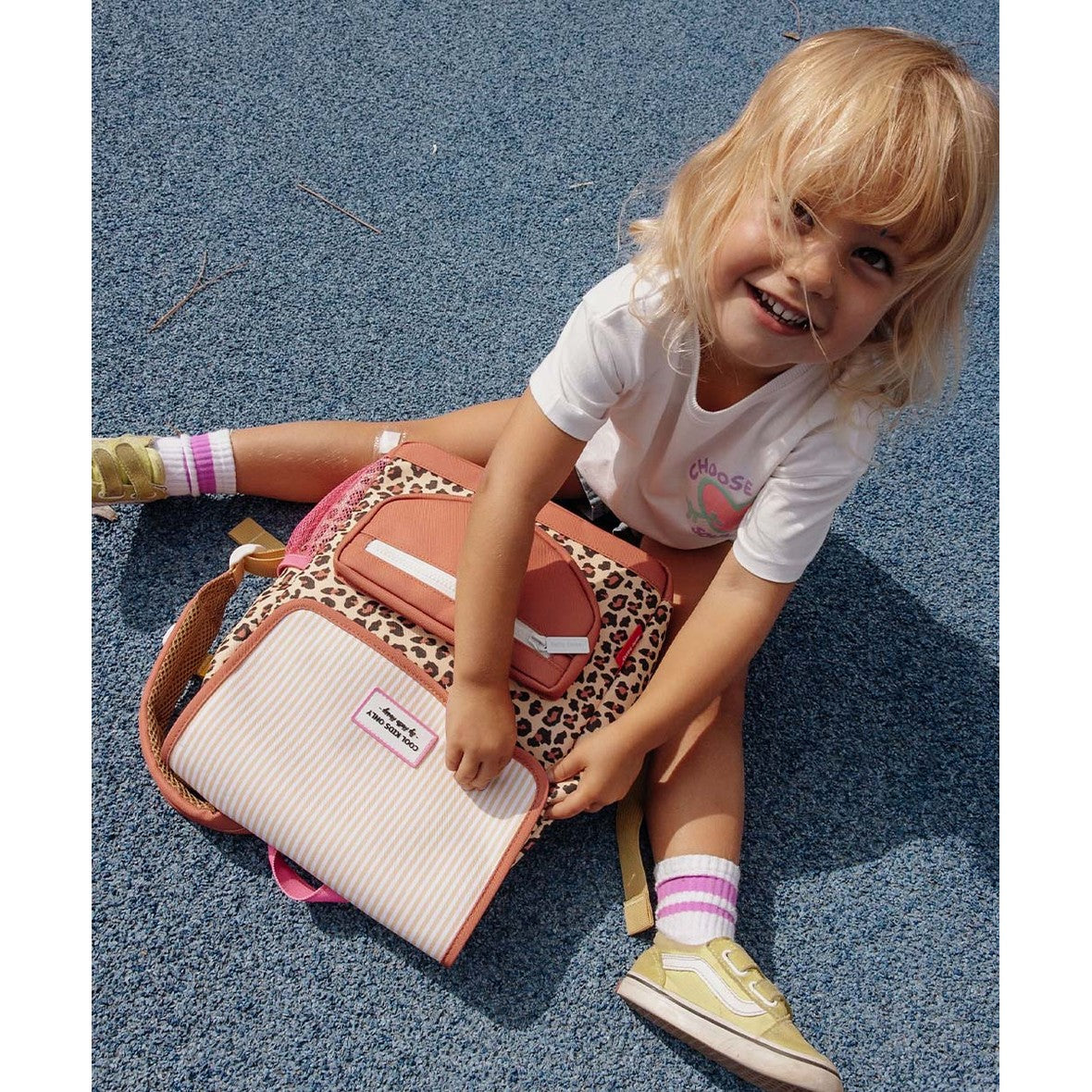 Maison Grenadine leopard print backpack next to girl on blue ground
