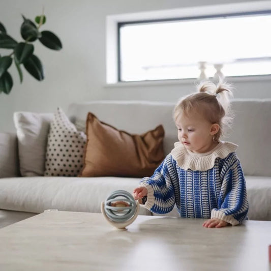 Toddler playing with La Mushie Suction Spinner Ball on wooden table