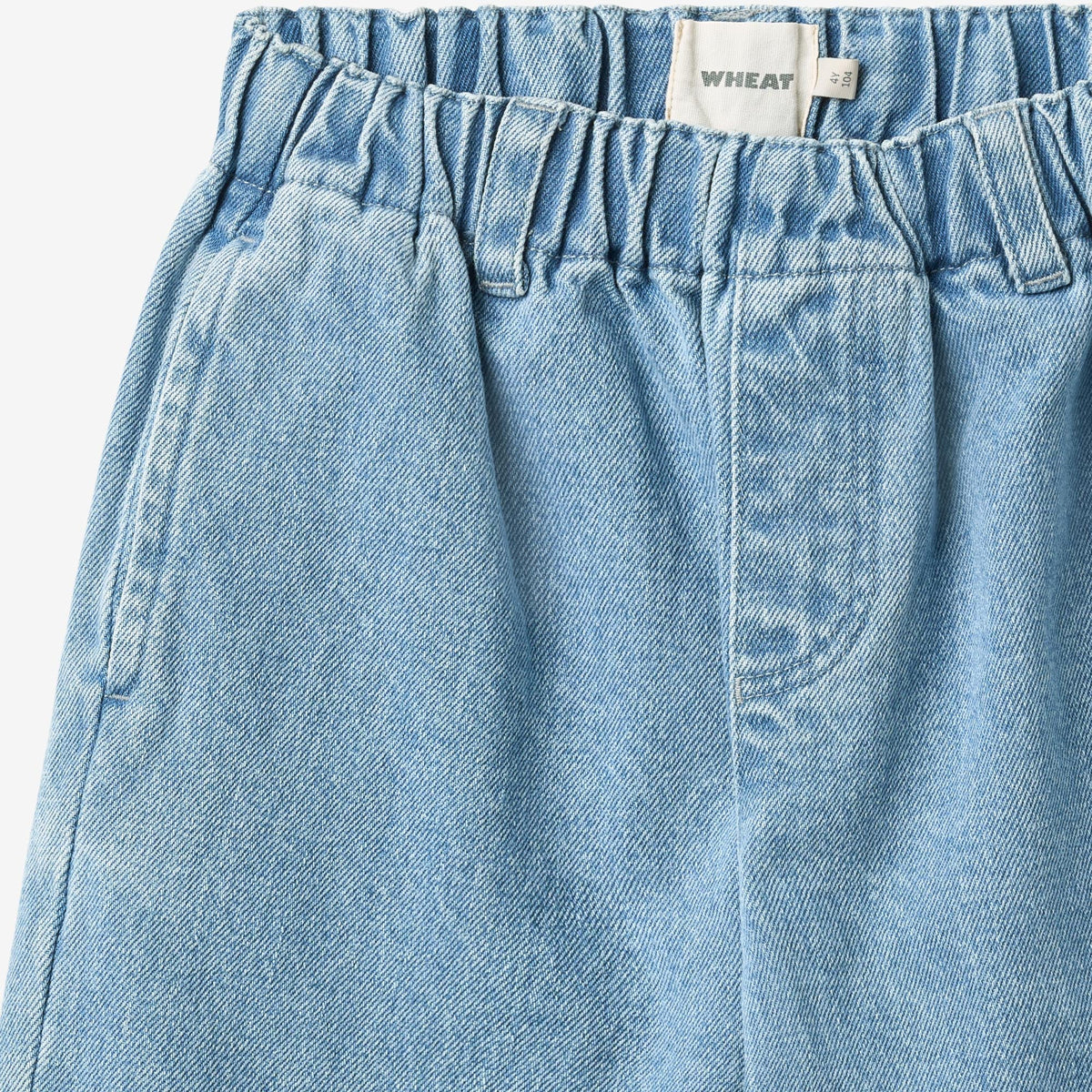 Close-up of WHEAT elasticated waistband, size tag, and light blue denim texture