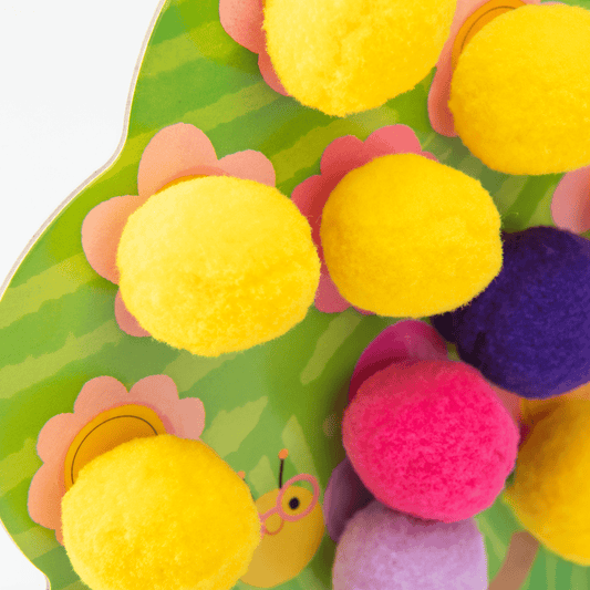Close-up of fuzzy yellow pink and purple felt pom-poms attached to green striped tree board
