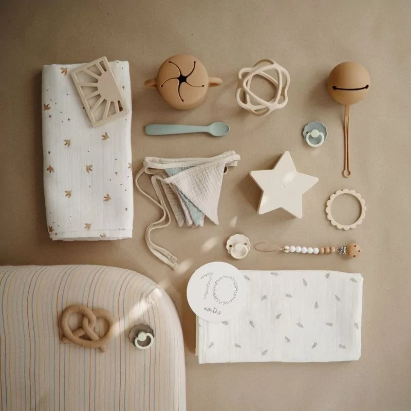 MUSHIES tan silicone pretzel teether with pacifier and baby accessories flat lay