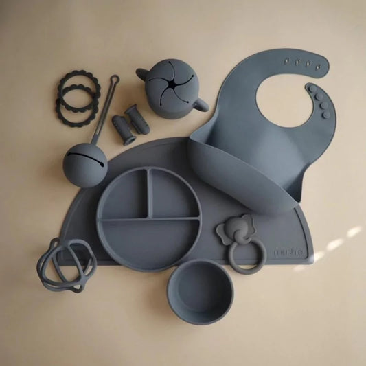 MUSHIES grey silicone baby essentials flat lay including teether, plate, and bib