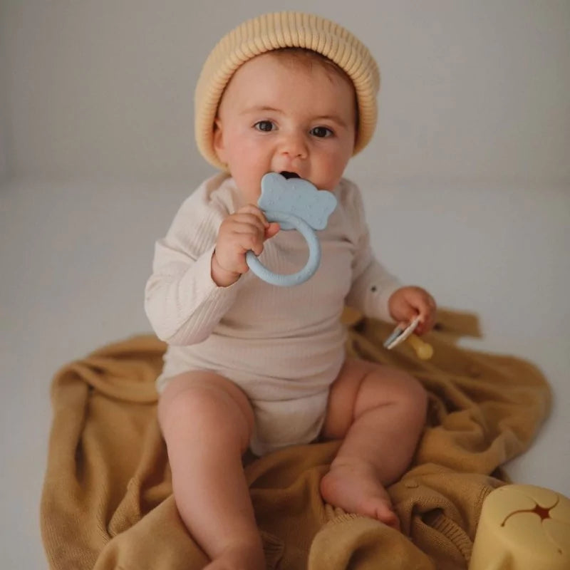 Baby using light blue cloud silicone teether while sitting on knit blanket