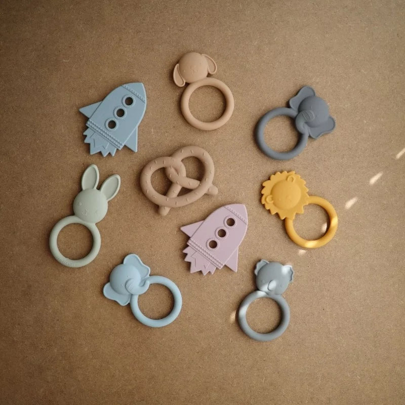 MUSHIES silicone teething ring set in pastel elephant, rocket, and bunny shapes