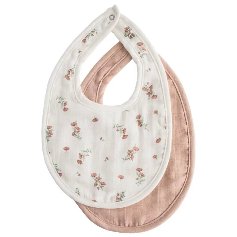 Close-up of layered white floral and solid blush muslin bibs highlighting neck snap details