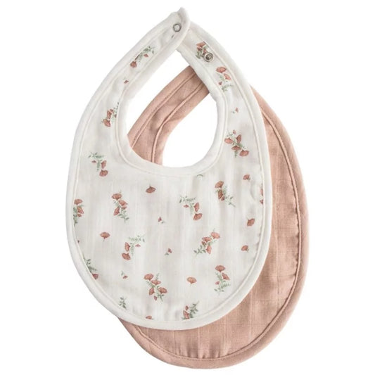 Close-up of layered white floral and solid blush muslin bibs highlighting neck snap details