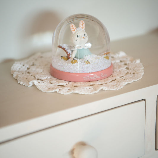 Moulin Roty snow globe decor item on cream lace doily on wooden dresser