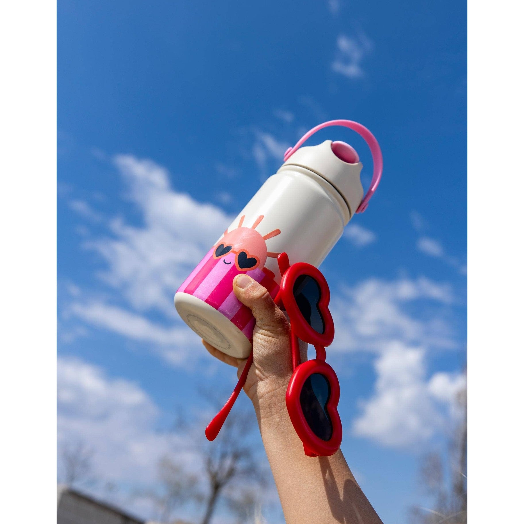 Pink striped kids bottle held against blue sky with heart sunglasses
