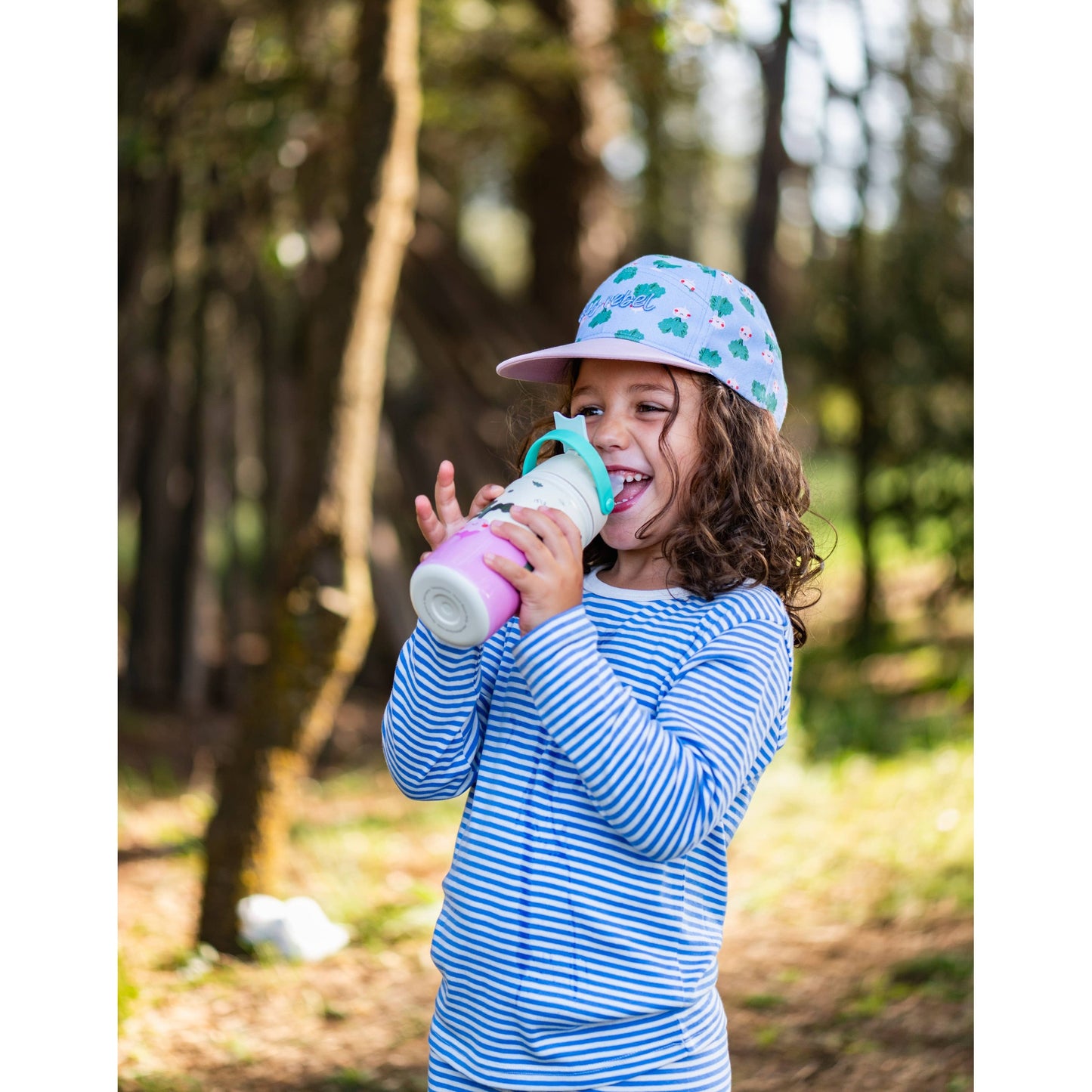 Girl drinking from pink and white insulated bottle outdoors