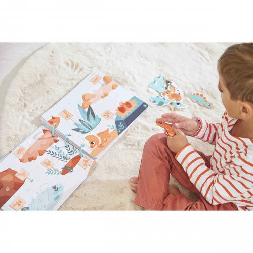 Toddler playing with colorful dinosaur busy book on rug with puzzle pieces