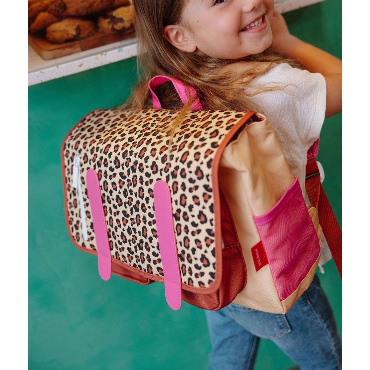 Girl smiling while wearing beige leopard print school bag over shoulder