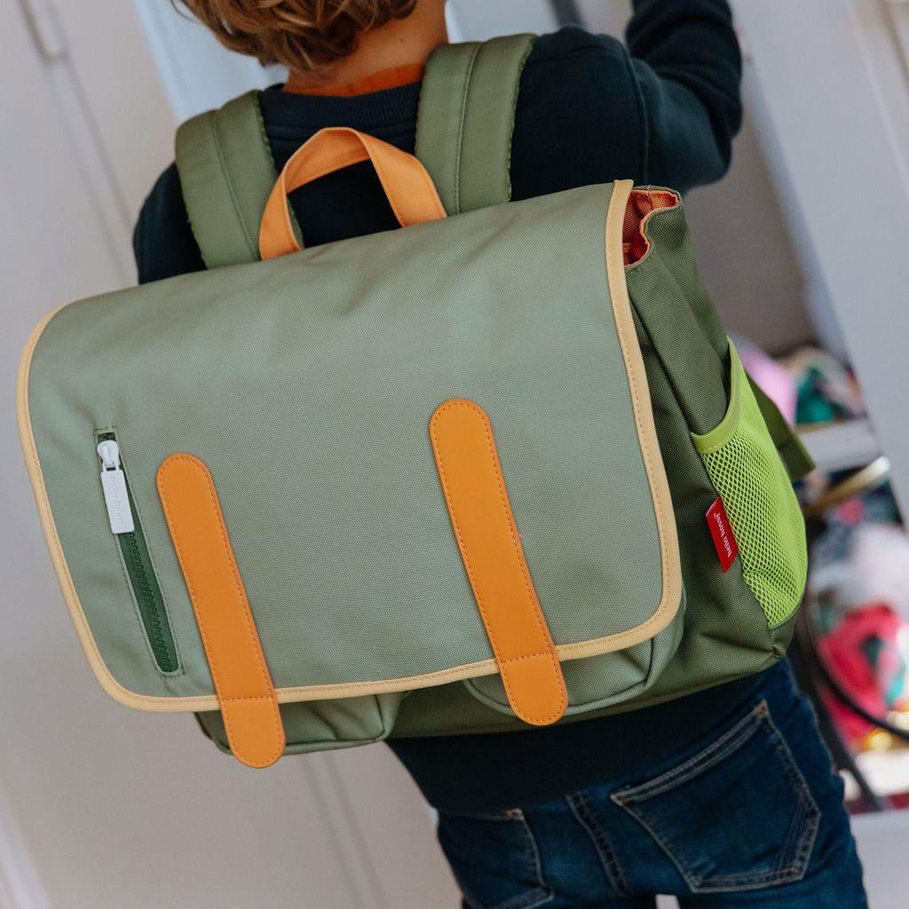Child wearing olive green Mini Safari backpack with red tag on side pocket