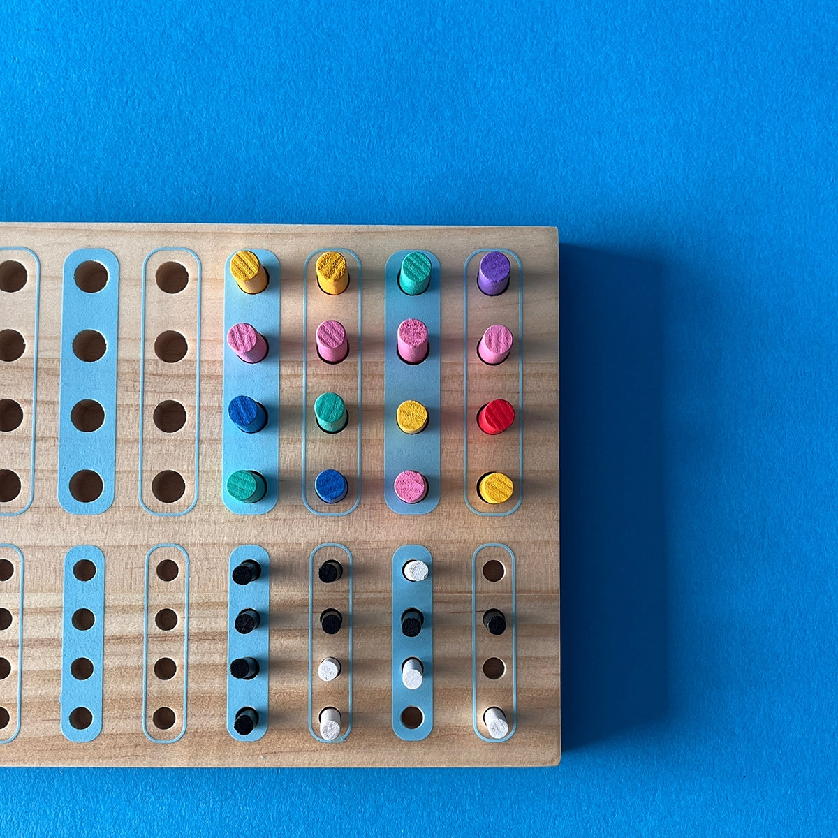 Close-up of wooden game board holes with yellow and teal colored pegs