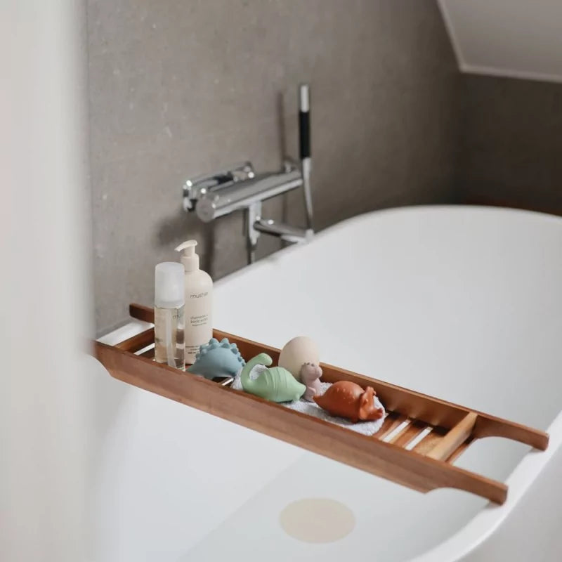 Blue, orange, and green silicone dinosaur bath toys on wooden tub caddy
