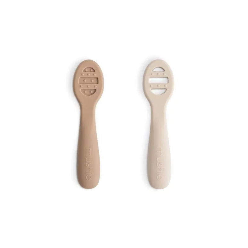 Close up of MUSHIES Shifting Sand and cream silicone baby spoons with ergonomic handle and textured sensory dots