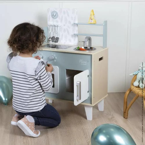 Child opening cabinet of wooden play kitchen with toy vegetables and balloons