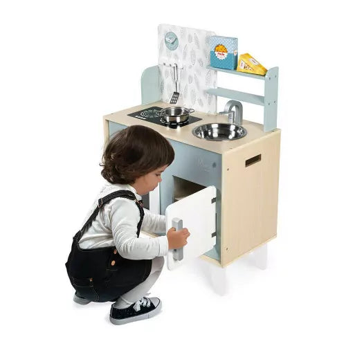 Child playing with wooden play kitchen featuring blue panel and hanging utensils