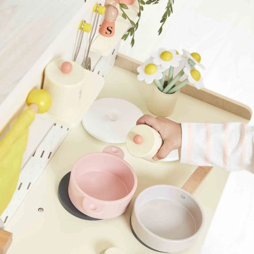 Close up of child hand using pink pot lid on wooden play kitchen counter