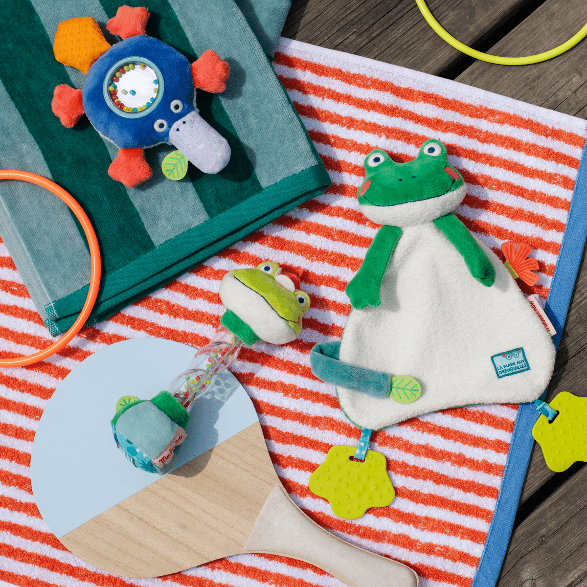 Green frog baby comforter styled with rattles and wooden toys on striped towel