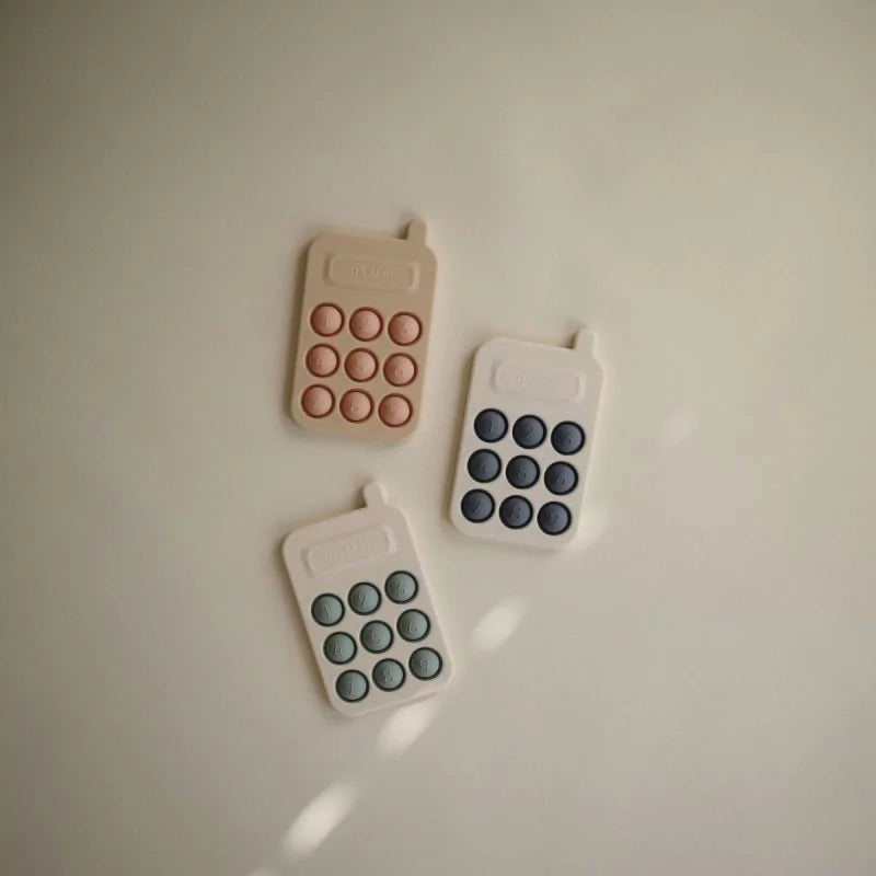 Set of three MUSHIES silicone baby phones in beige, navy, and sage colors