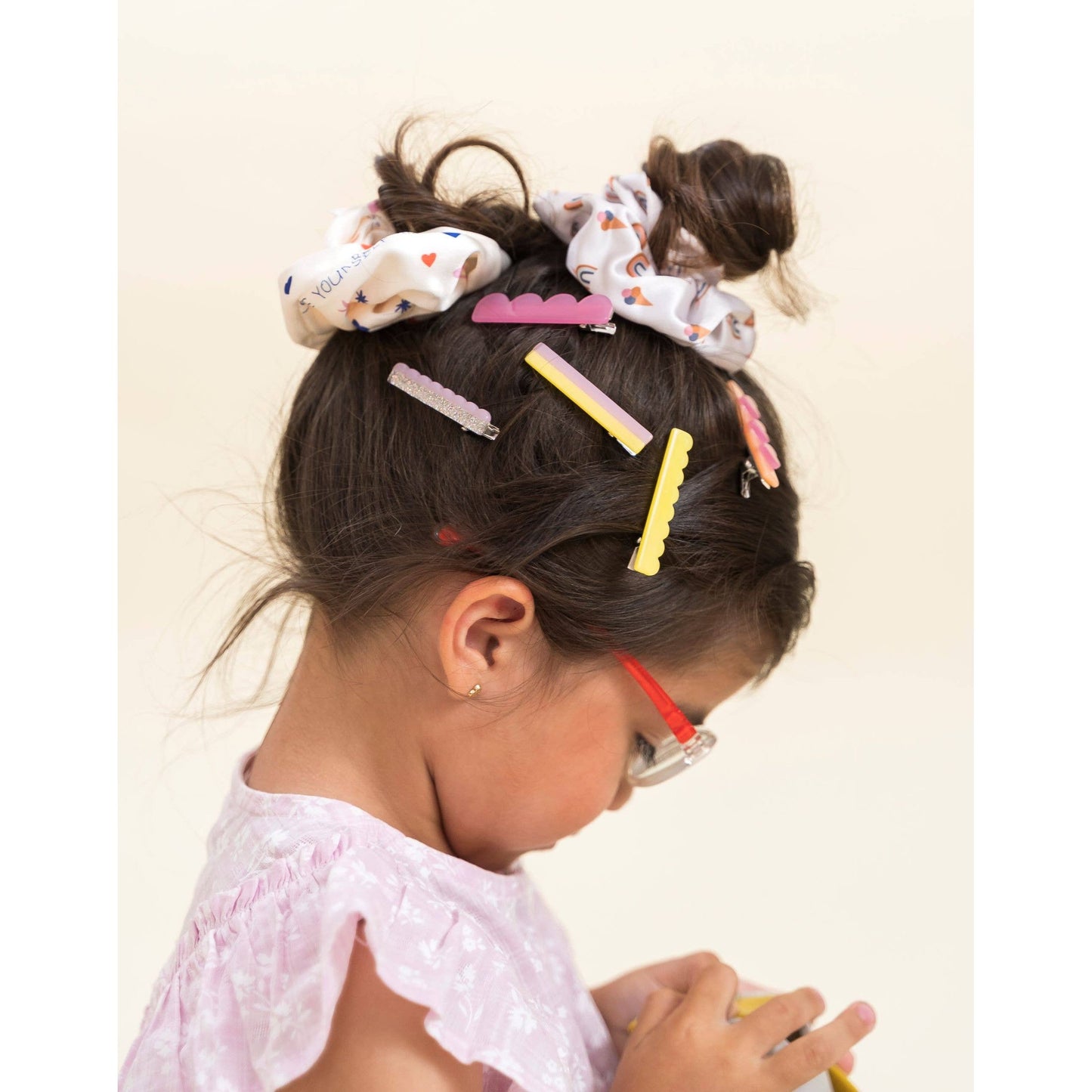 Girl with dark brown half-up hair styled with pink scalloped, yellow glitter, and layered acetate clips