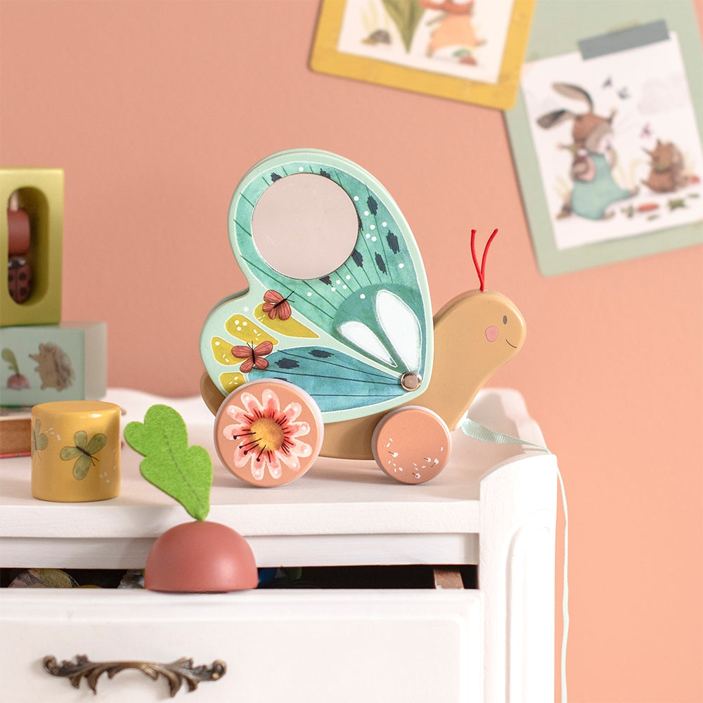Lifestyle shot of wooden butterfly pull toy on white drawer unit surrounded by children's toys