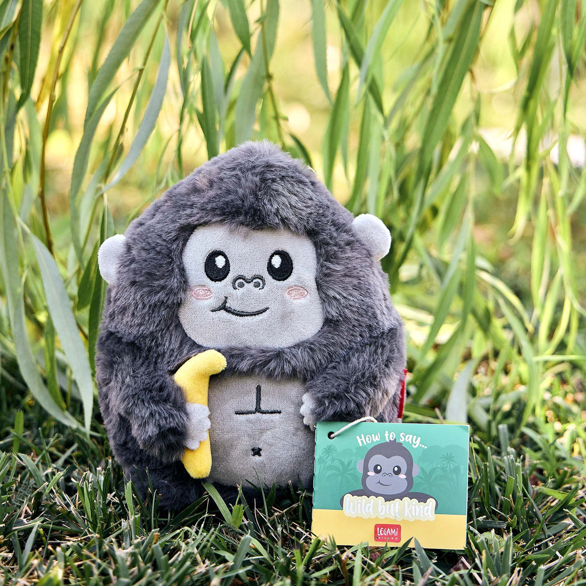 Small grey plush gorilla in grass with 'Wild but Kind' ID tag