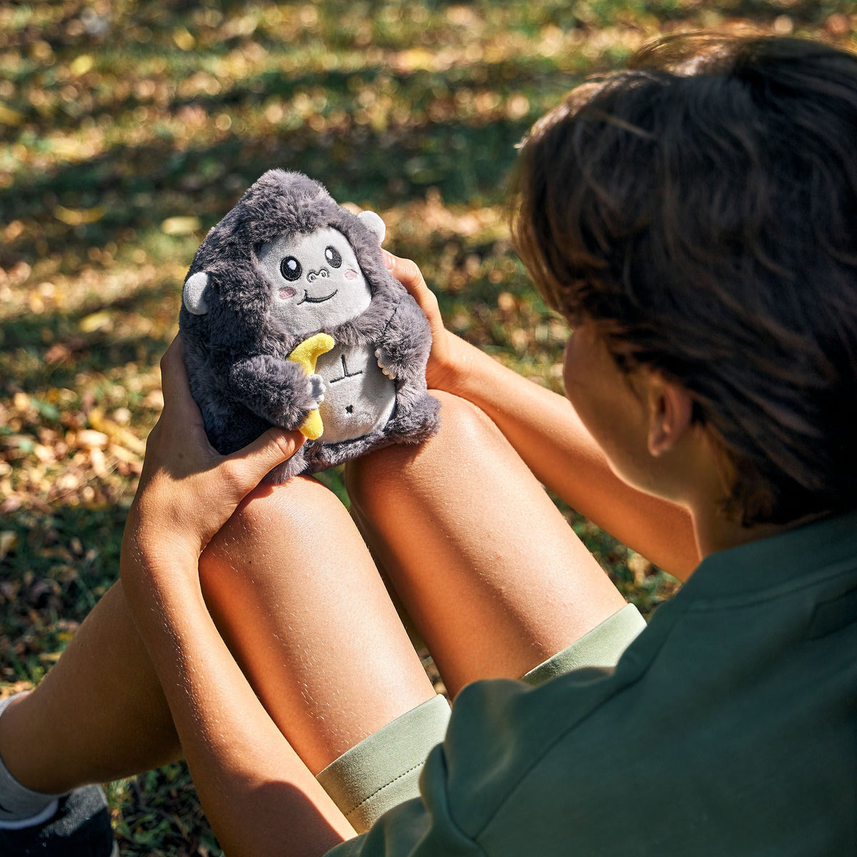 Person holding small grey plush gorilla outdoors on grass