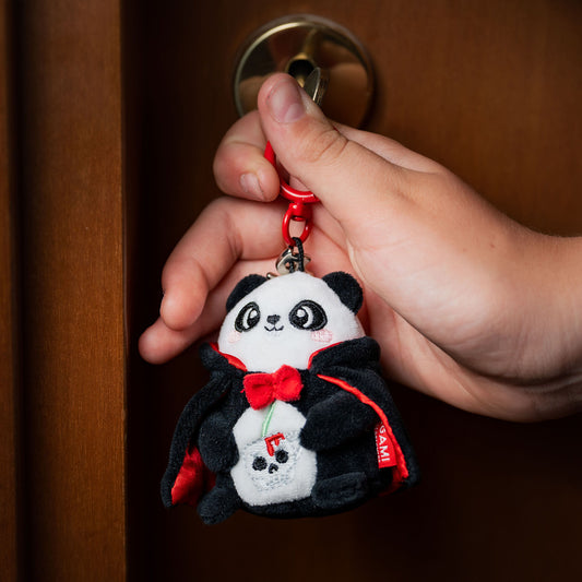 Hand holding Halloween panda keychain against wooden door