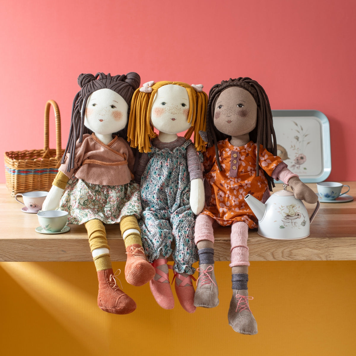 Three Camelia dolls with yarn hair styled in buns, braids, and pigtails on wooden surface