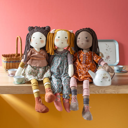 Three Camelia dolls with yarn hair styled in buns, braids, and pigtails on wooden surface