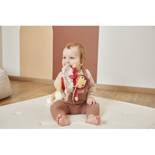 Baby holding soft Kaloo Émilie fabric doll with red headband and heart skirt