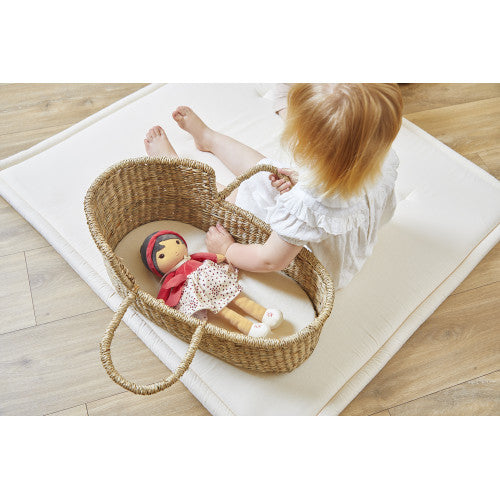 Child reaching for Kaloo Émilie plush doll in wicker bassinet
