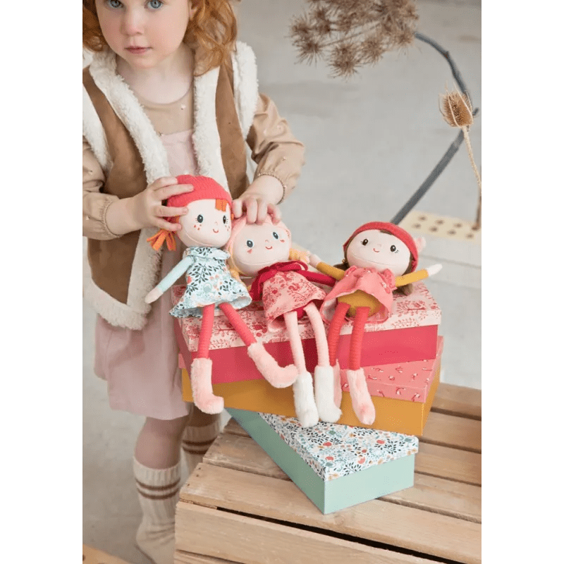 Child holding Lilliputiens Stella fabric doll with other dolls displayed on stacked gift boxes