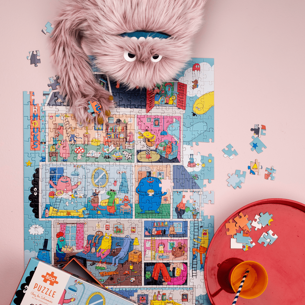 Child assembling the 500-piece Les Schmouks puzzle with loose pieces and pink puppet on pink surface