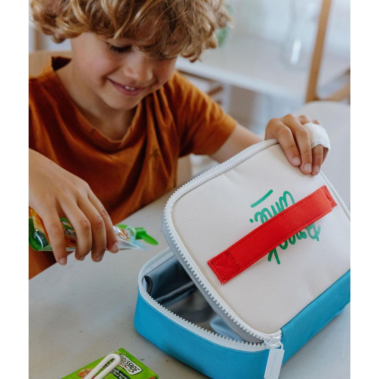 Child packing snack into blue and cream insulated lunch bag