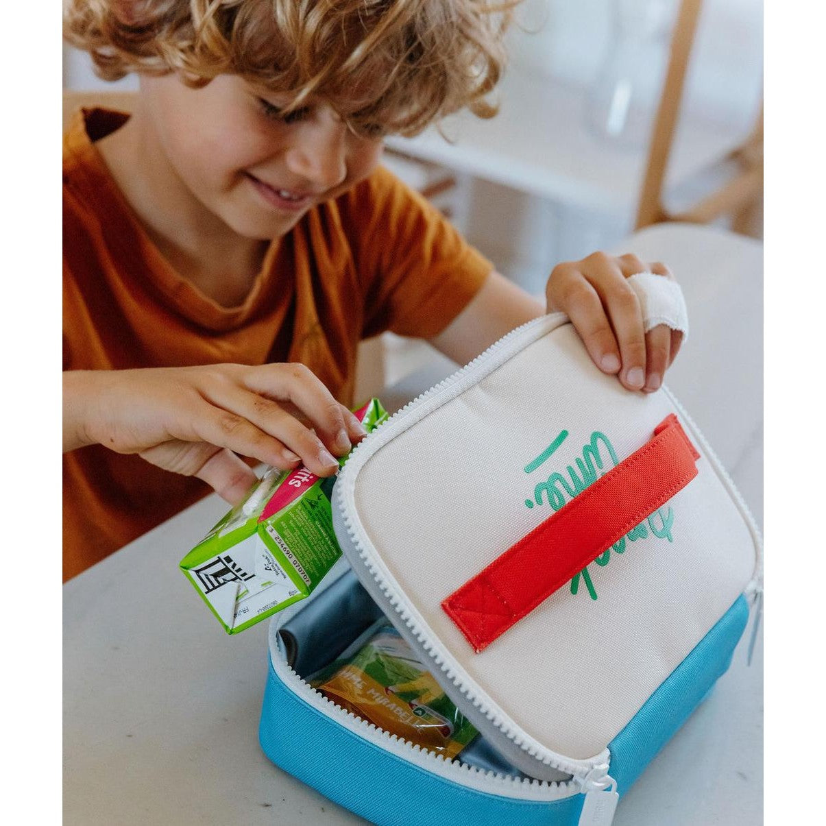 Child placing juice box in blue and cream insulated lunch bag