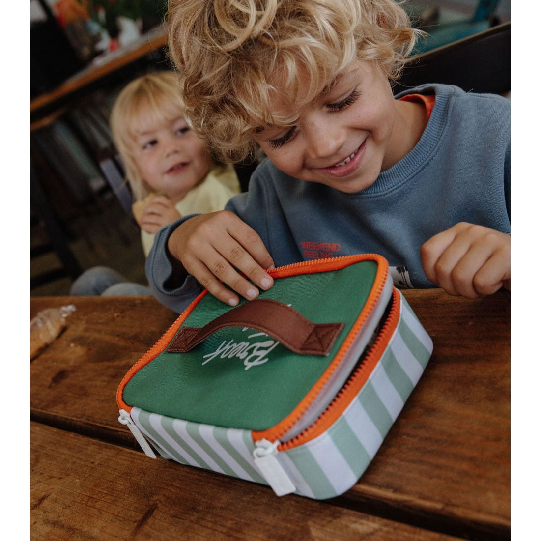 Child unzipping green striped insulated lunch bag with brown handle