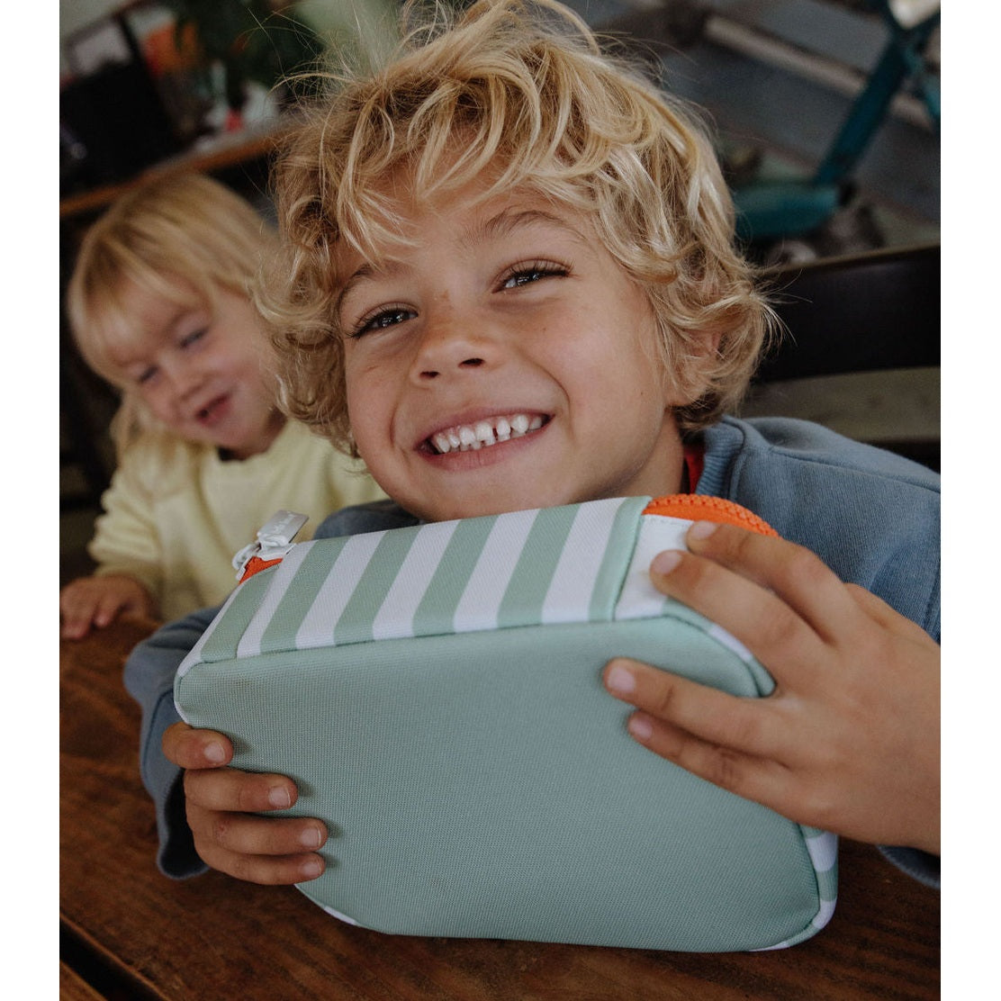 Close-up of child holding green striped insulated lunch bag with orange zipper