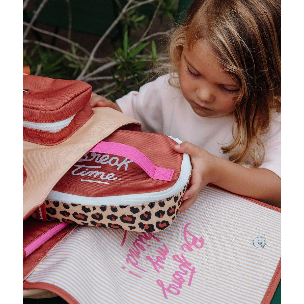 Child placing leopard print lunch bag into backpack outdoors