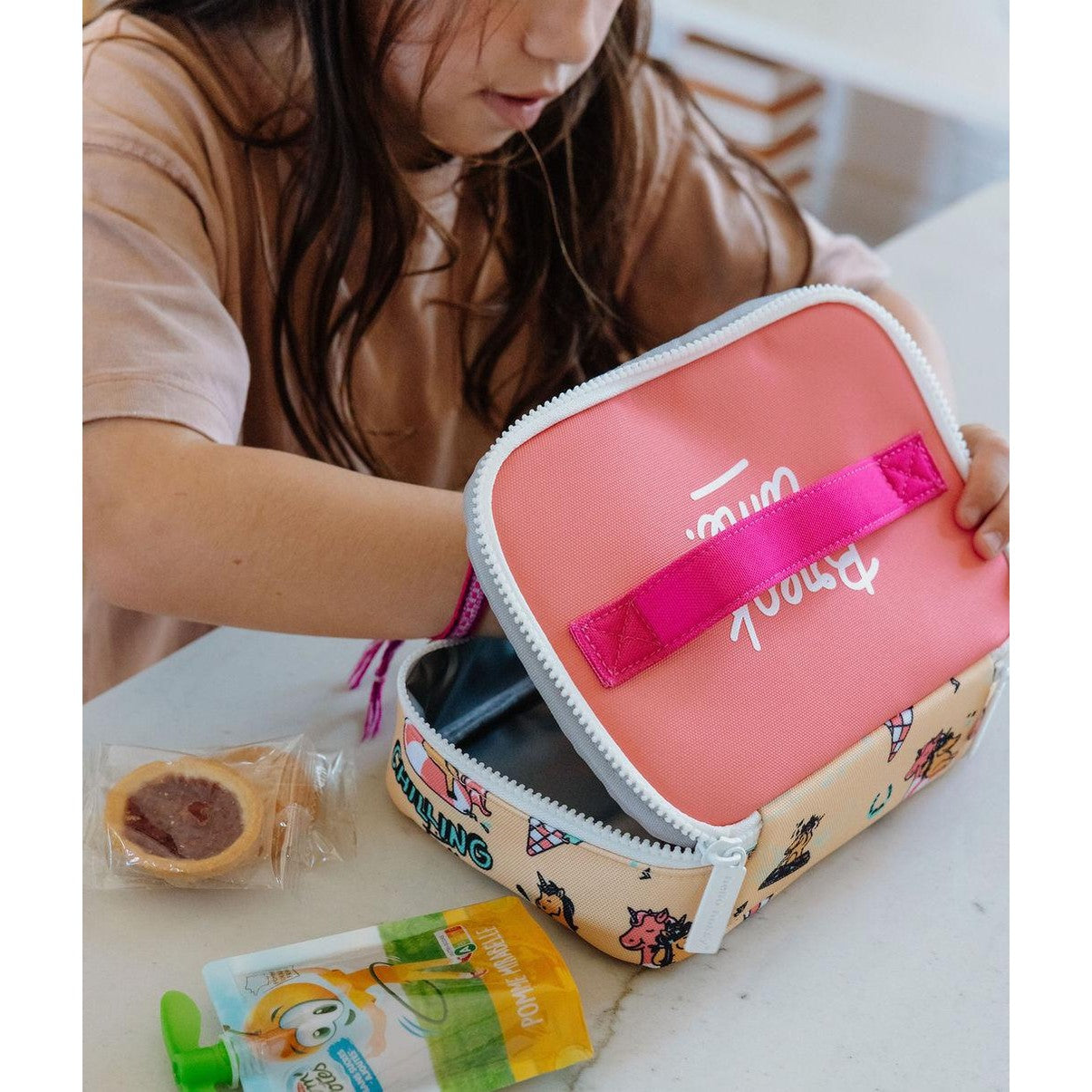 Girl holding open unicorn lunch bag with food and juice pouch inside