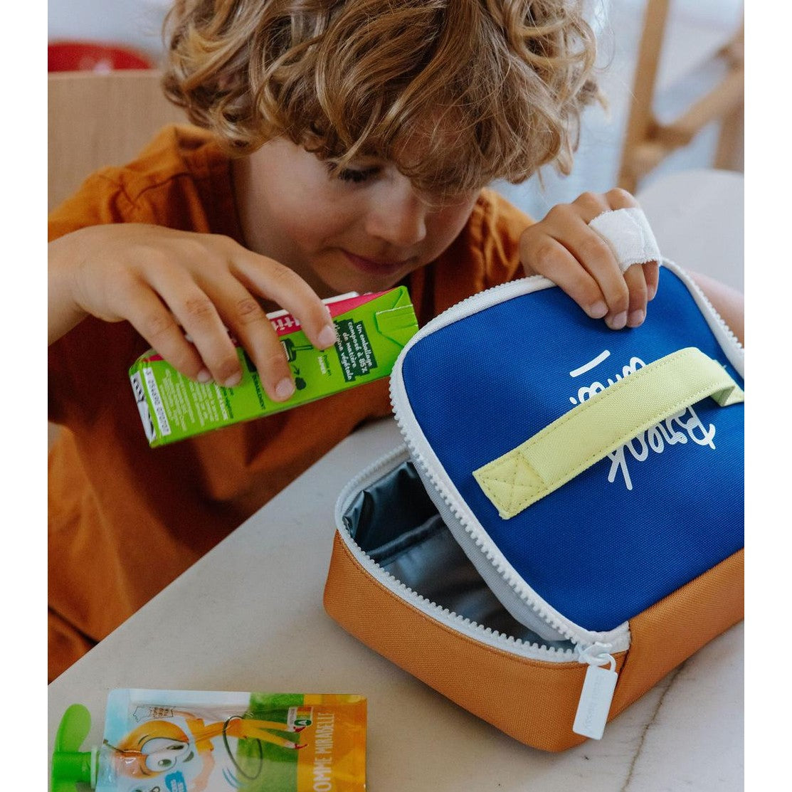 Child placing juice box into blue and orange insulated lunch bag