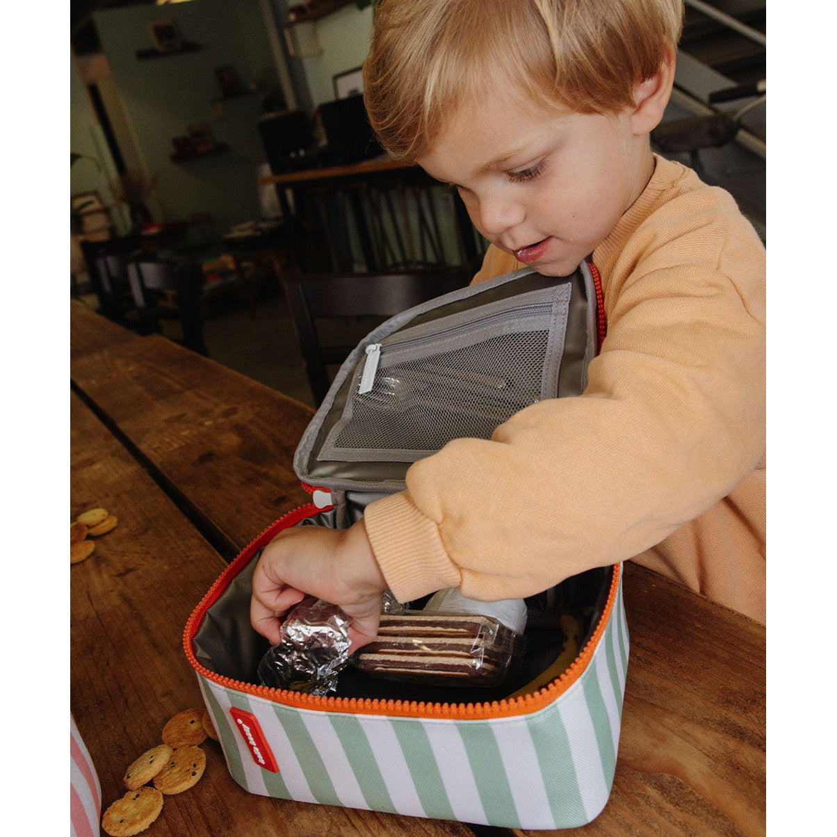 Child packing snacks into green striped insulated lunch bag